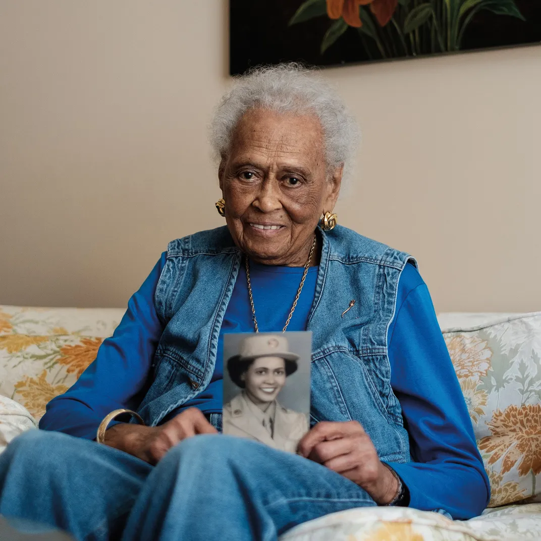 An elderly Black woman holds a portrait of herself while in uniform during world war two